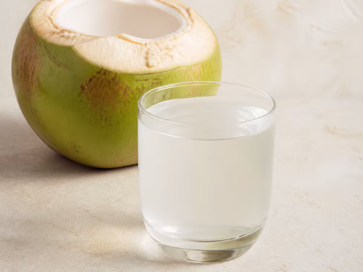 Agua de coco natural en un vaso junto a un coco verde abierto
