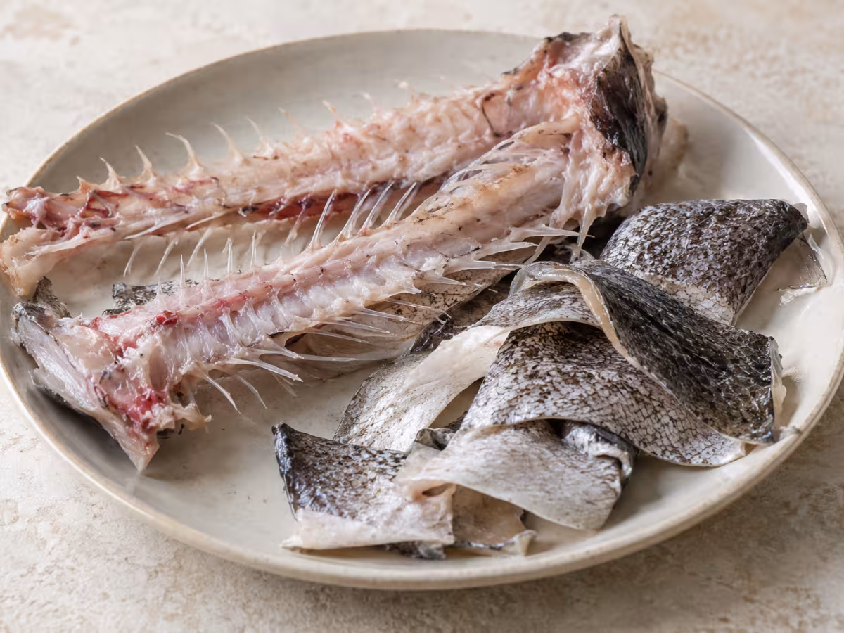 Espinas y pieles de merluza sobre superficie de cocina, sin preparar
