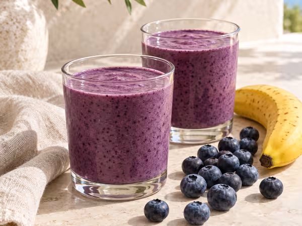 Dos vasos de Batido de ar&aacute;ndanos y pl&aacute;tano con sus ingredientes frescos