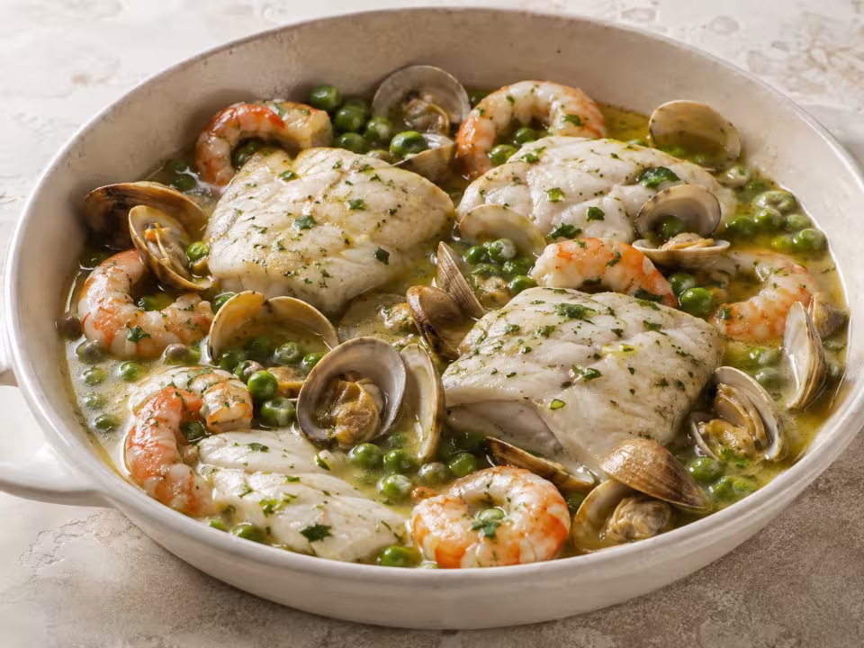 Merluza con almejas y langostinos presentado en una mesa clara