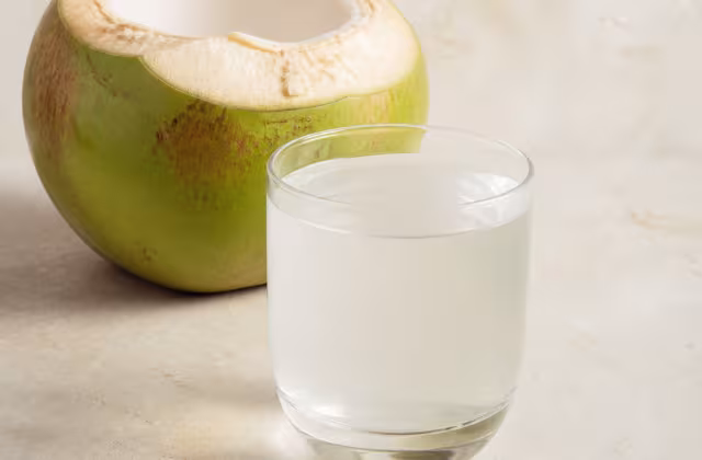 Agua de coco natural en un vaso junto a un coco verde abierto