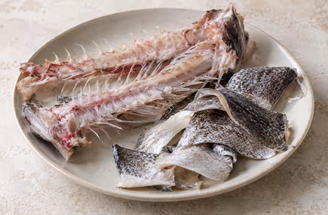 Espinas y pieles de merluza sobre superficie de cocina, sin preparar